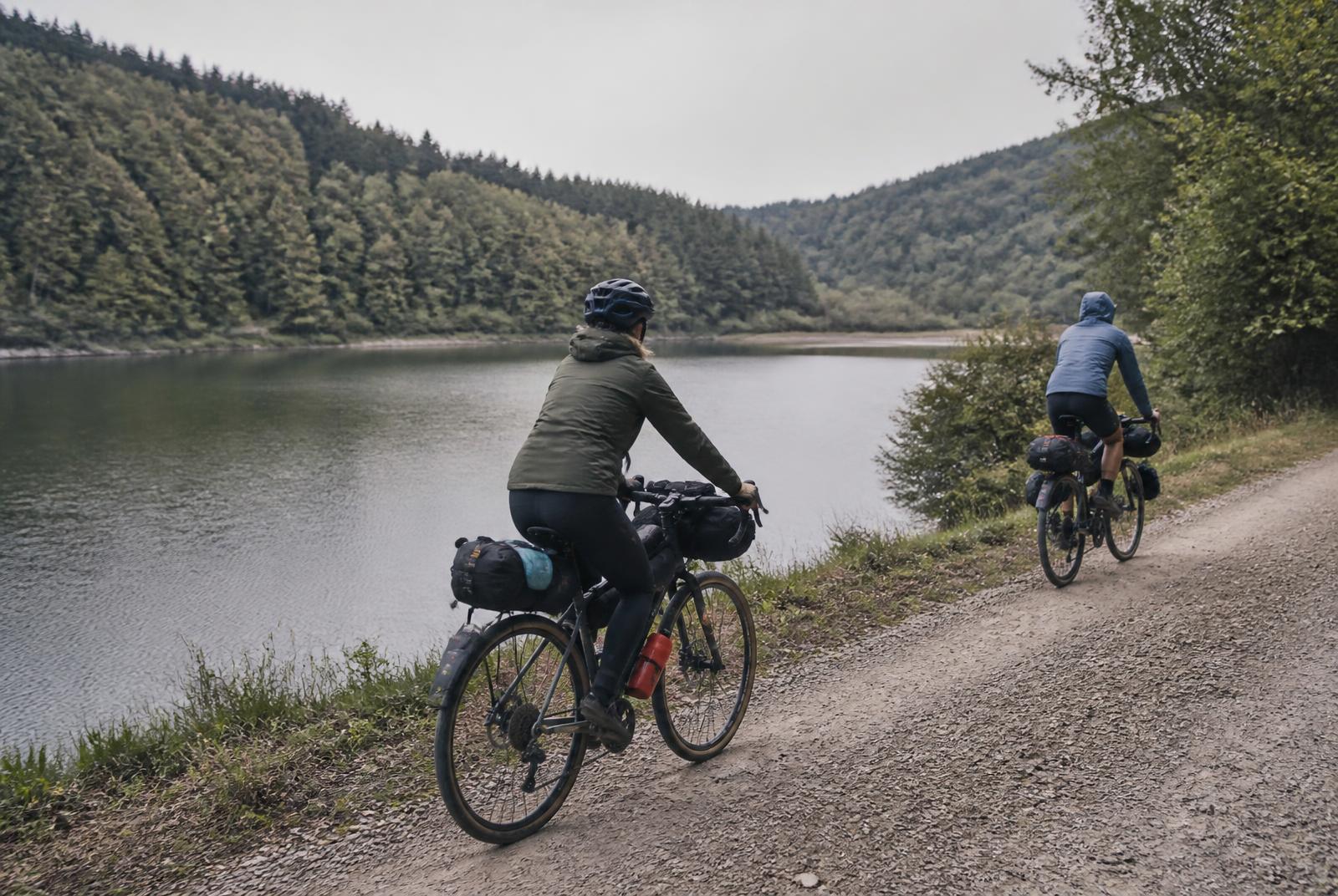 Zwei Bikepacker auf einem ruhigen Weg entlang eines Waldsees