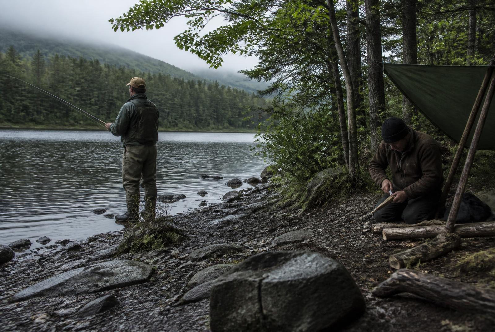 Angler und Bushcrafter bei ihren Tätigkeiten an einem Waldsee